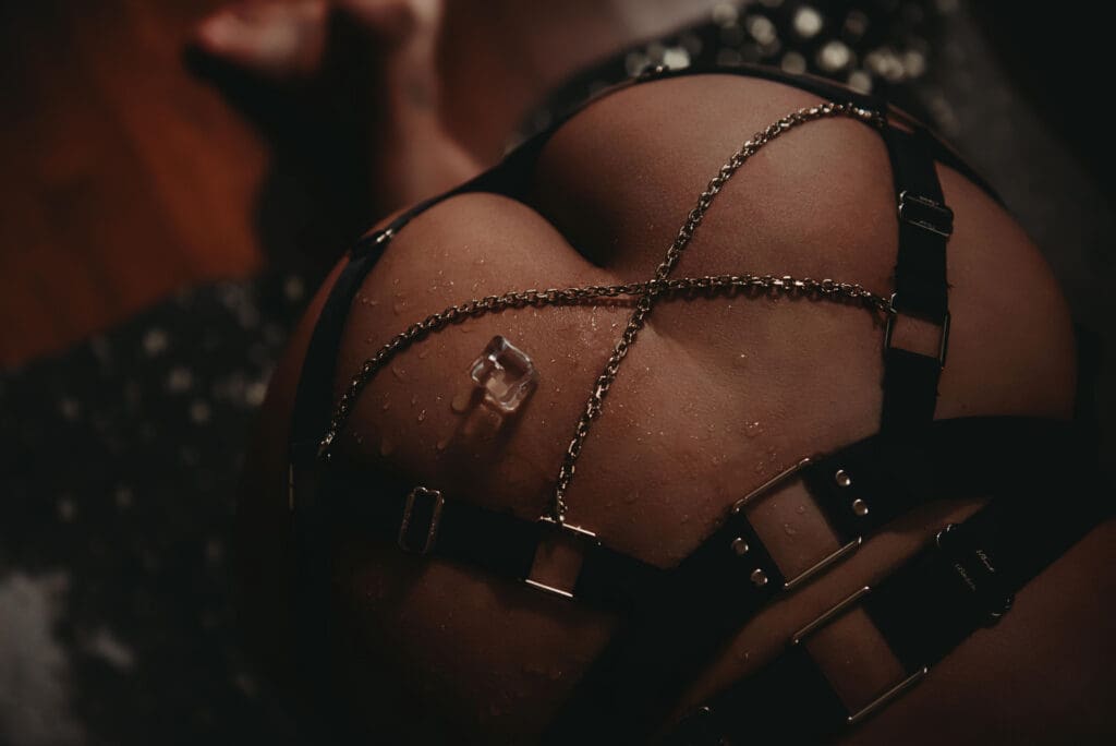Bold boudoir portrait in Deland, FL — detail of a chain and leather harness against skin in moody low light.